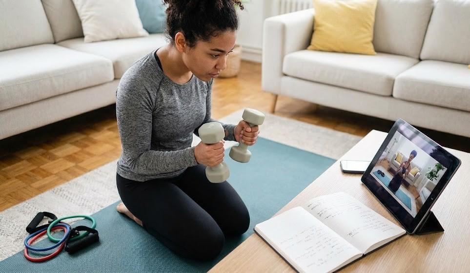 Image showing a lady following an online workout while lifting dumbbells at home